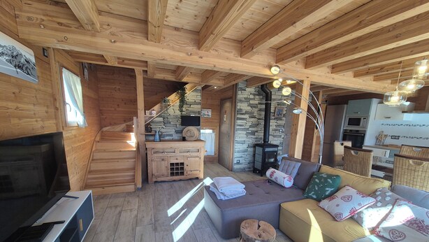 A cozy cabin interior with a wooden ceiling, stone wall, and a fireplace. There is a sofa, a small table, and a TV. - Exceptional Chalet for Rent in La Féclaz – 4 Bedrooms, Sleeps 10** (Les Deserts)