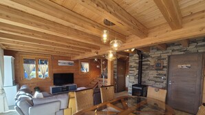 A wooden cabin interior with a living area, sofa, glass-top table, stone wall, and a fireplace. - Exceptional Chalet for Rent in La Féclaz – 4 Bedrooms, Sleeps 10** (Les Deserts)