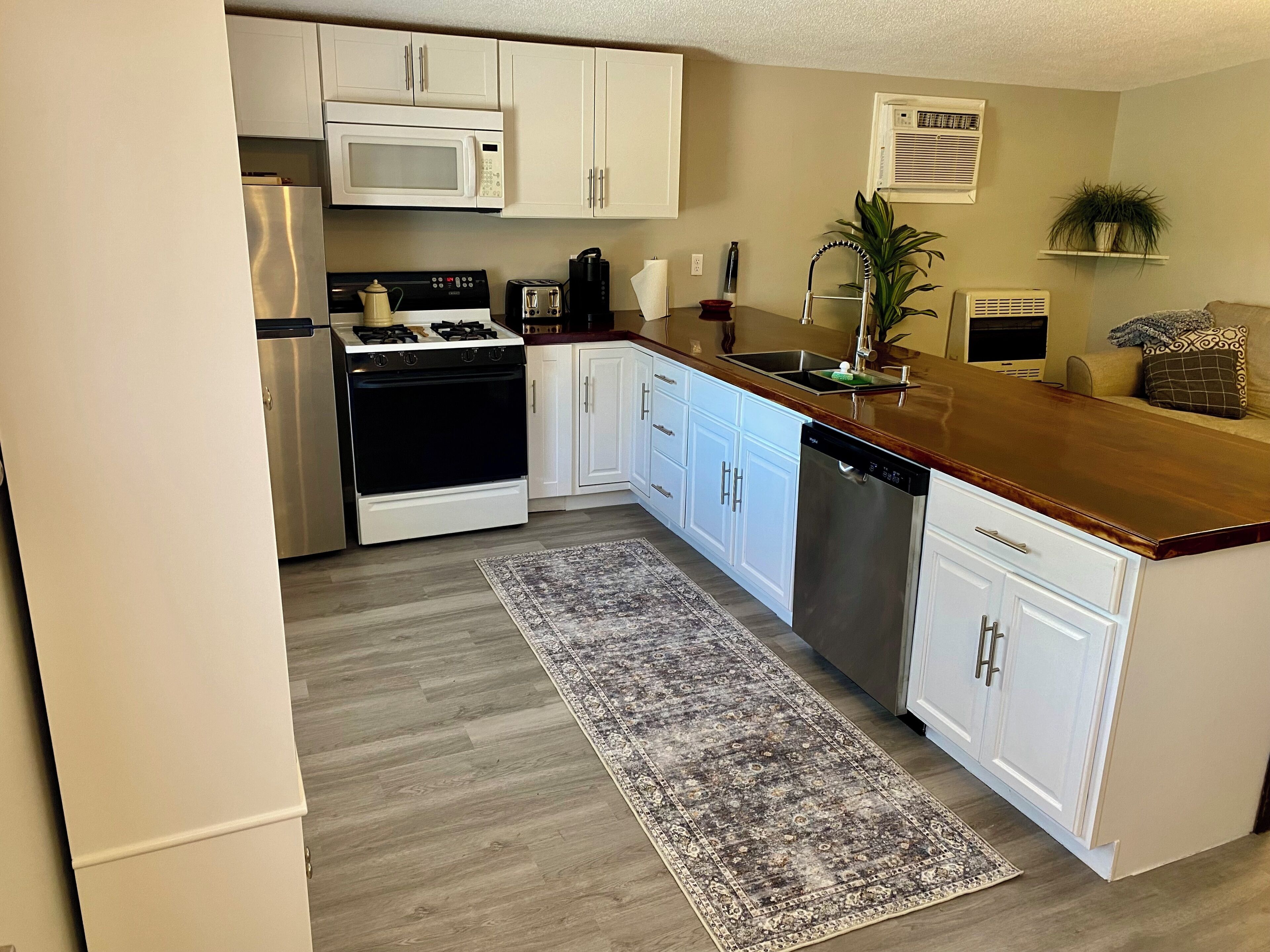 A kitchen with white cabinets, a stainless steel dishwasher, a microwave, a stove, and a coffee maker.