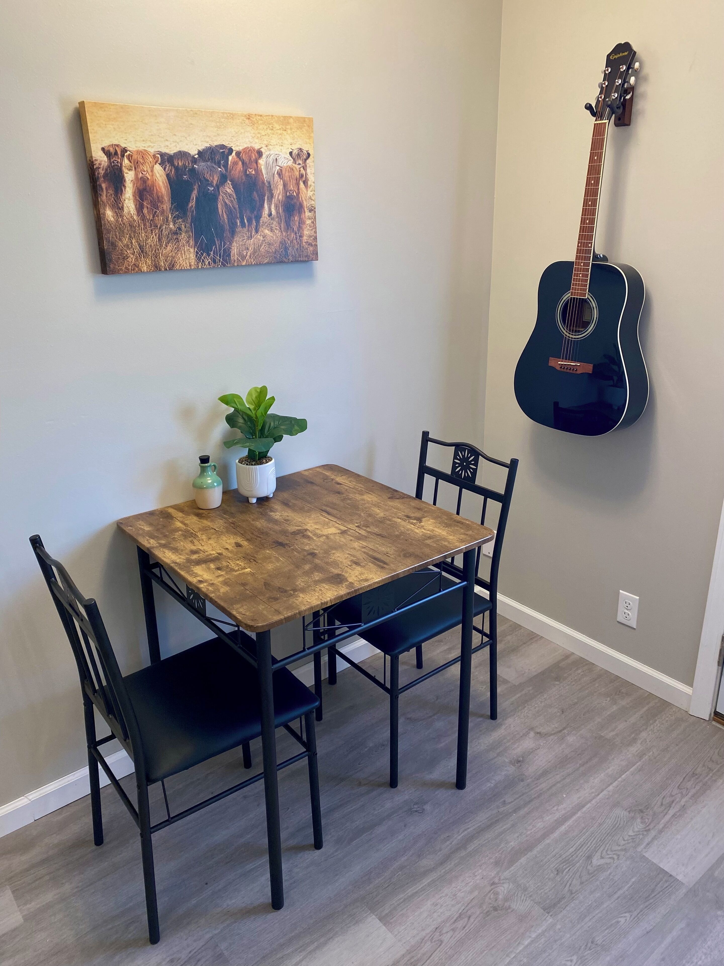 A dining area with a wooden table, four chairs, a potted plant, and a guitar on the wall.