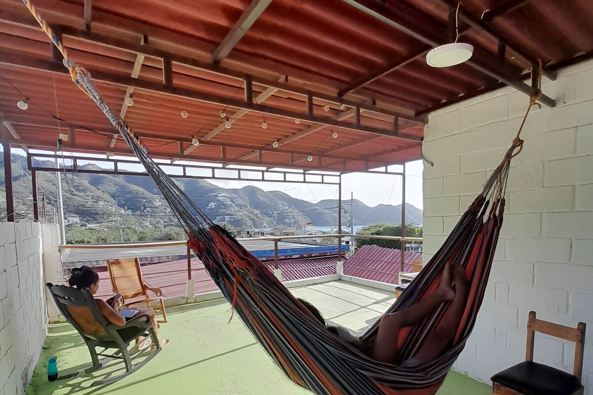 Una hamaca colgada del techo en una habitación con vistas a montañas. Hay dos mecedoras y una pequeña mesa de madera.