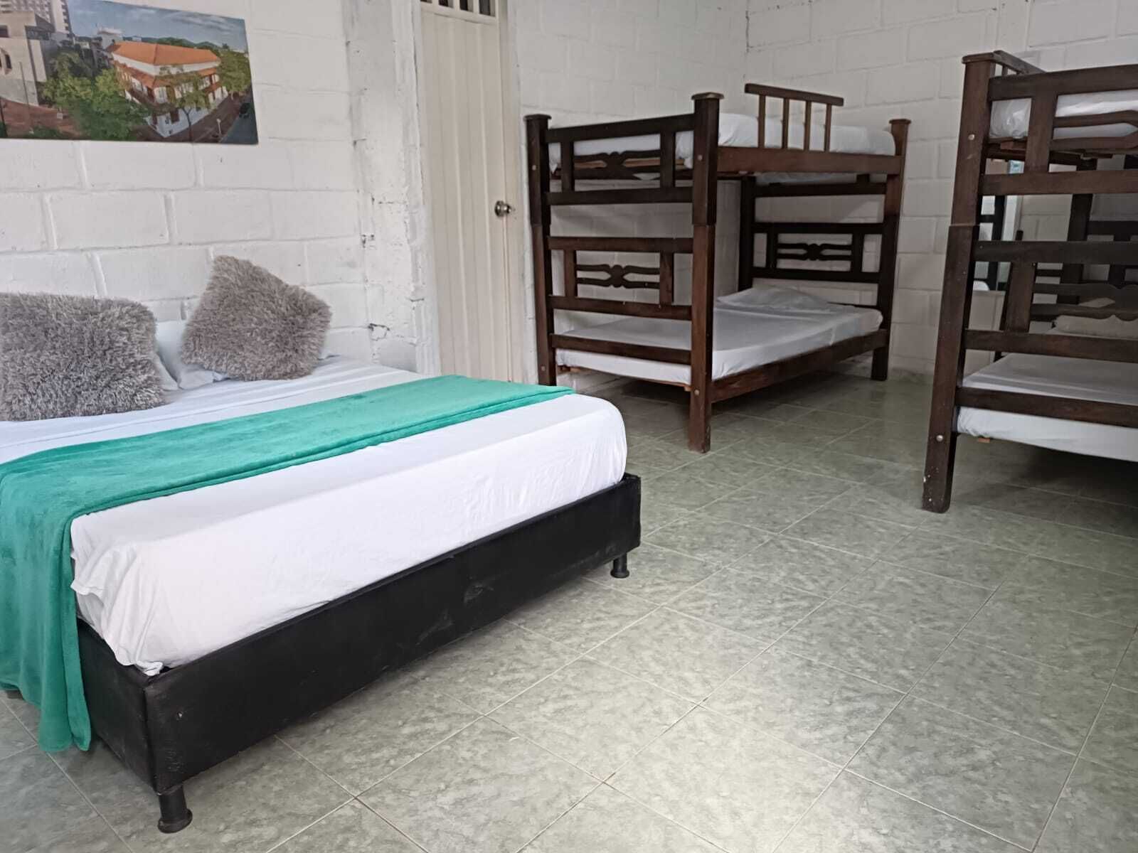 Een kamer met een enkel bed, twee stapelbedden en een witte bakstenen muur met een afbeelding.