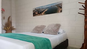 A bedroom with a bed, a green blanket, two fluffy pillows, a painting on the wall, and a wooden chair. - Taganga Tropical House (Santa Marta)