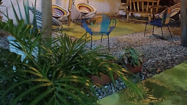 An outdoor patio area with rustic wooden furniture, including chairs and a table. There are potted plants and a small garden area with pebbles. - Taganga Tropical House (Santa Marta)