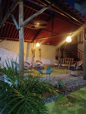 Un espace extérieur aménagé en terrasse, avec des meubles en bois rustique, notamment des chaises et une table. On y trouve également des plantes en pot et un petit jardin agrémenté de galets.
