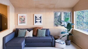 A modern living room with a sectional sofa, two pendant lights, and a large window with a view of trees.
