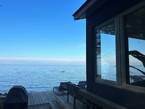 A wooden deck with a grill, a chair, and a table overlooking a calm body of water. - Cozy Cabin on the shore of Georgian Bay. Truly a hidden gem! (Meaford)