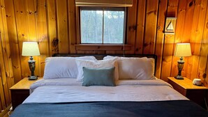 A wooden-paneled room with a bed, two bedside lamps, and a window. - Charming 3-bedroom lakefront house with large yard and sandy beach (Colchester)