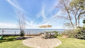 A patio with a table and chairs, an umbrella, and a view of a lake. - Charming 3-bedroom lakefront house with large yard and sandy beach (Colchester)