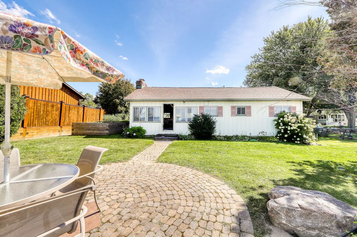 Una casa amb un camí pavimentat que condueix a la porta principal, una tanca de fusta i una zona de pati amb taula i cadires.