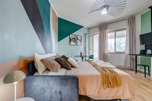 Quarto de hotel moderno com cama, mesa de cabeceira, luminária e televisão.