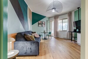 Uma sala de estar moderna com sofá, uma mesa pequena, televisão e área de cozinha.