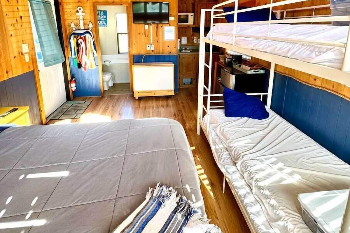A cabin interior with a wooden ceiling, a ceiling fan, a bunk bed, a desk with a computer, and a television.
