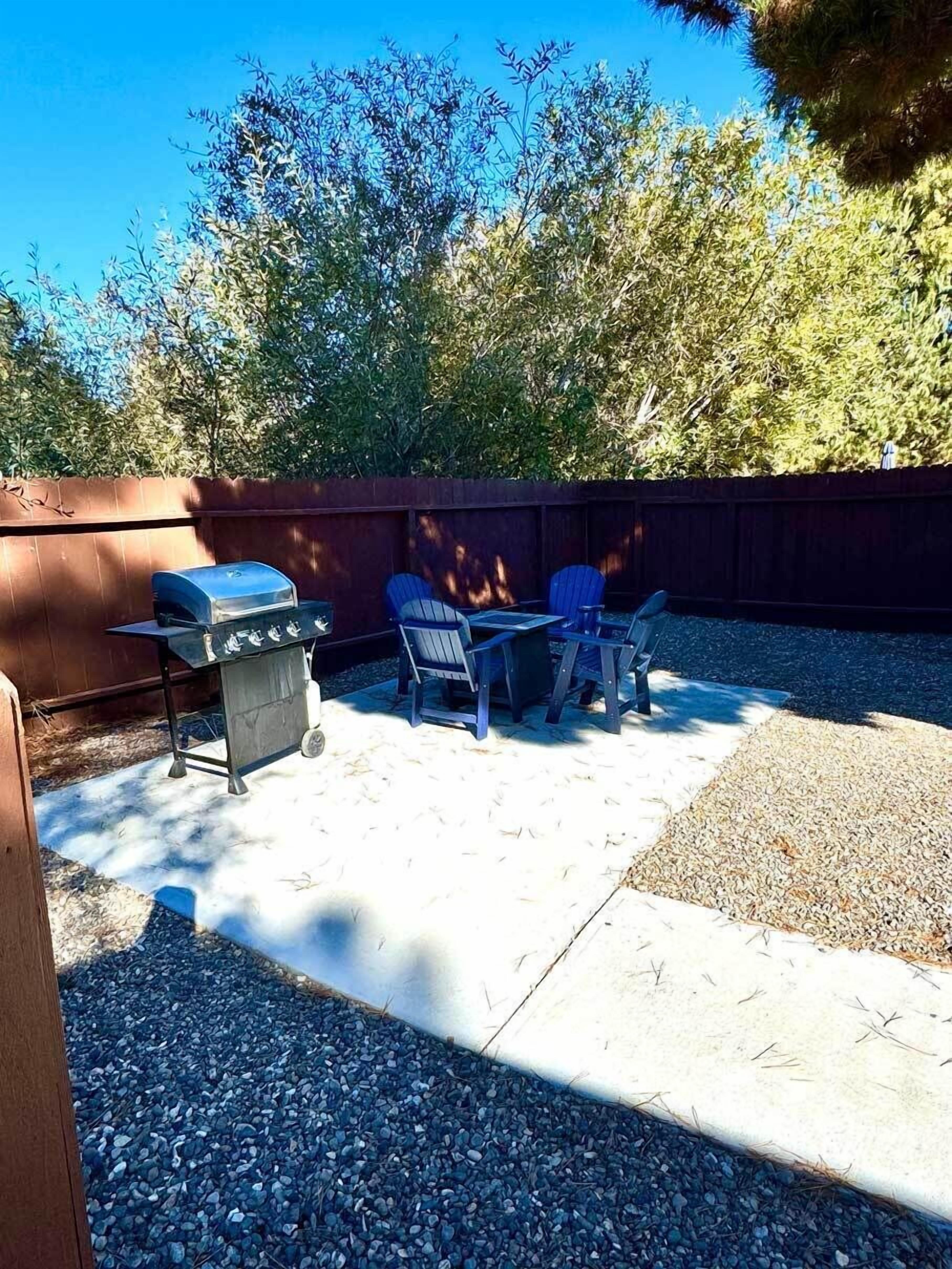 An outdoor patio with a barbecue grill, two Adirondack chairs, and a table.