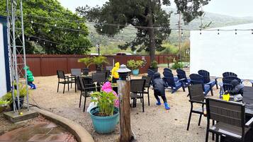 Un patio al aire libre con mesas y sillas, rodeado de plantas en macetas y una valla de madera.