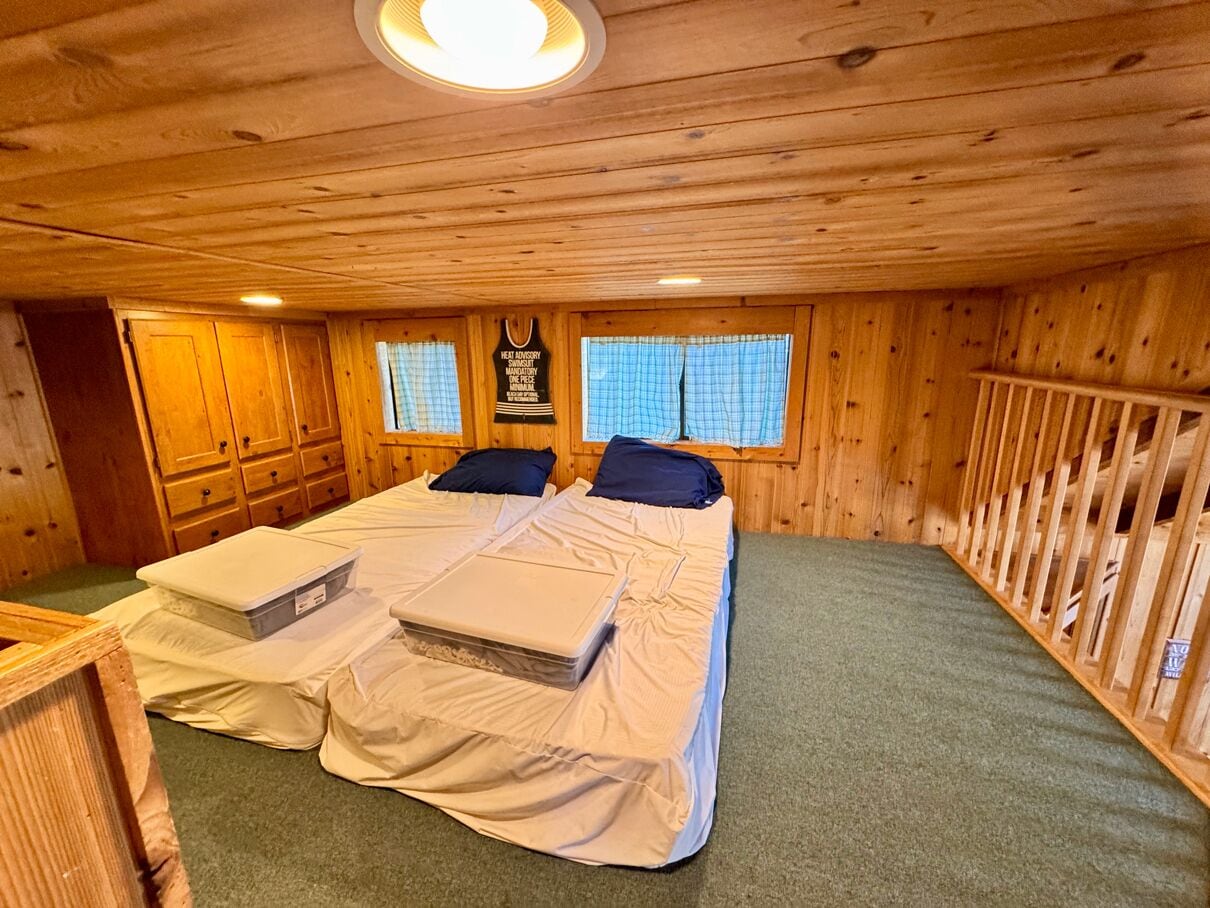 A wooden cabin bedroom with two beds, a small window, and a wooden ceiling.
