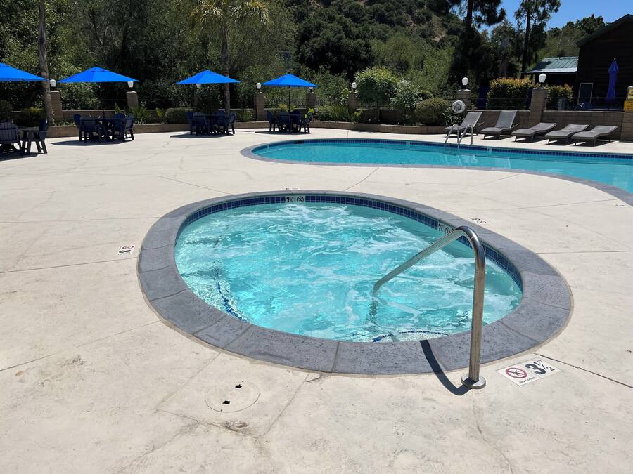 A swimming pool with a hot tub, lounge chairs, and umbrellas.