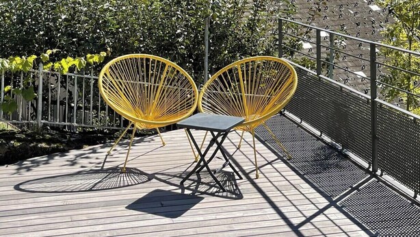 A terrace with yellow chairs, a metal fence, and a mountainous backdrop.