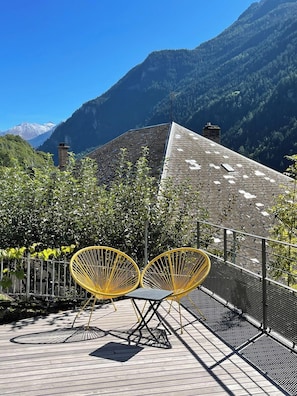 A terrace with yellow chairs, a metal fence, and a mountainous backdrop. - Le Repère des Cerfs - access to Val Thorens (Orelle)