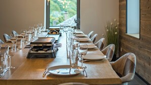 A dining area with a long table set for a meal, a view of mountains through a large window, and a modern wooden wall.