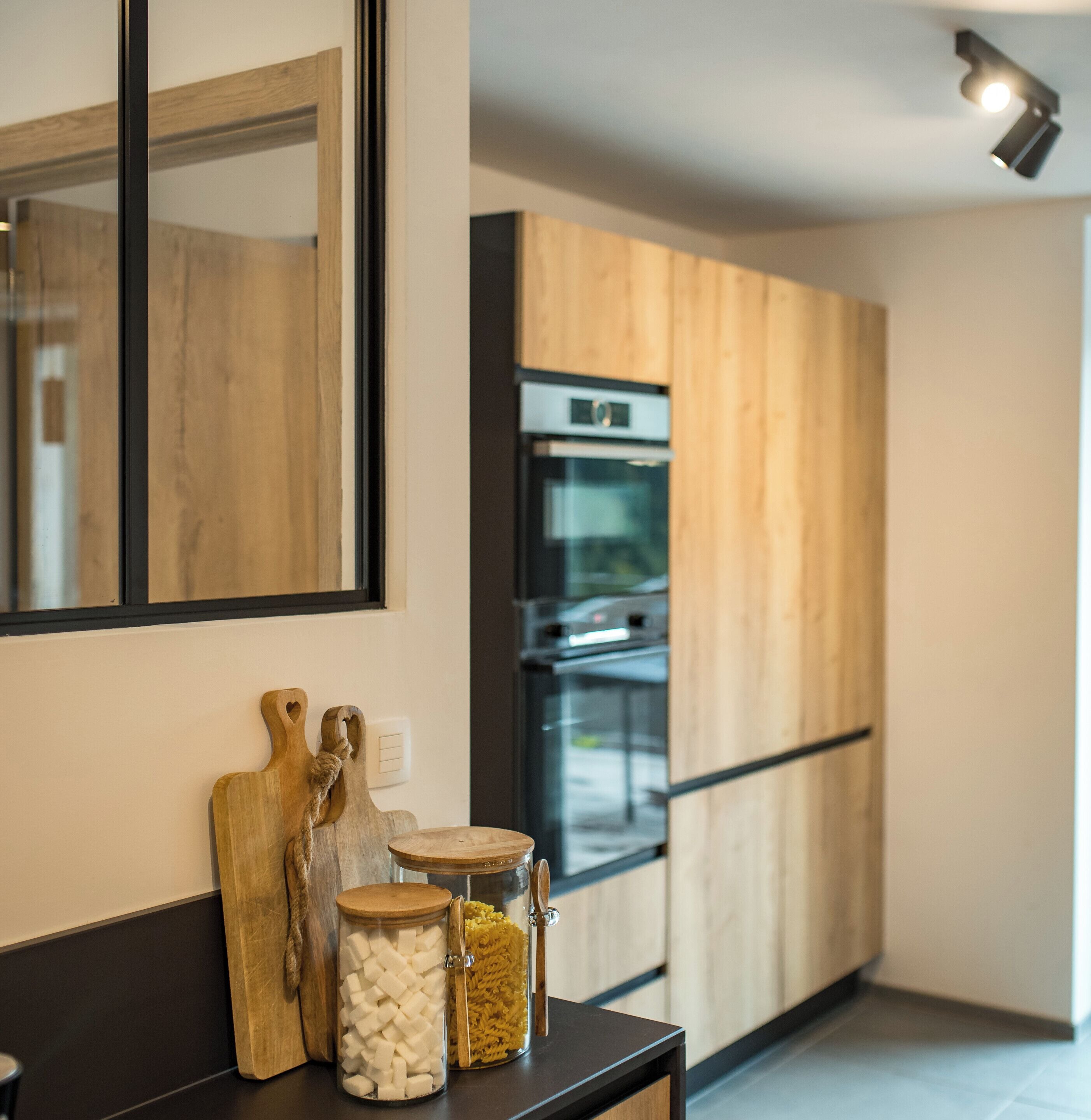 Une cuisine moderne avec des meubles en bois, un four encastré et deux bocaux posés sur un plan de travail noir.