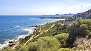 A coastal landscape with a clear view of the sea, a winding path, and a row of buildings along the hillside. - Porto Corallo Two-room apartment 4 beds (Villaputzu)