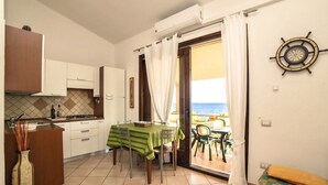 A compact kitchen with a dining area, a view of the sea through a sliding door, and a ship's wheel decoration on the wall. - Porto Corallo Two-room apartment 4 beds (Villaputzu)