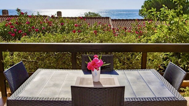 A patio with a table and chairs, a vase of flowers, and a view of the sea. - Porto Corallo Two-room apartment 4 beds (Villaputzu)