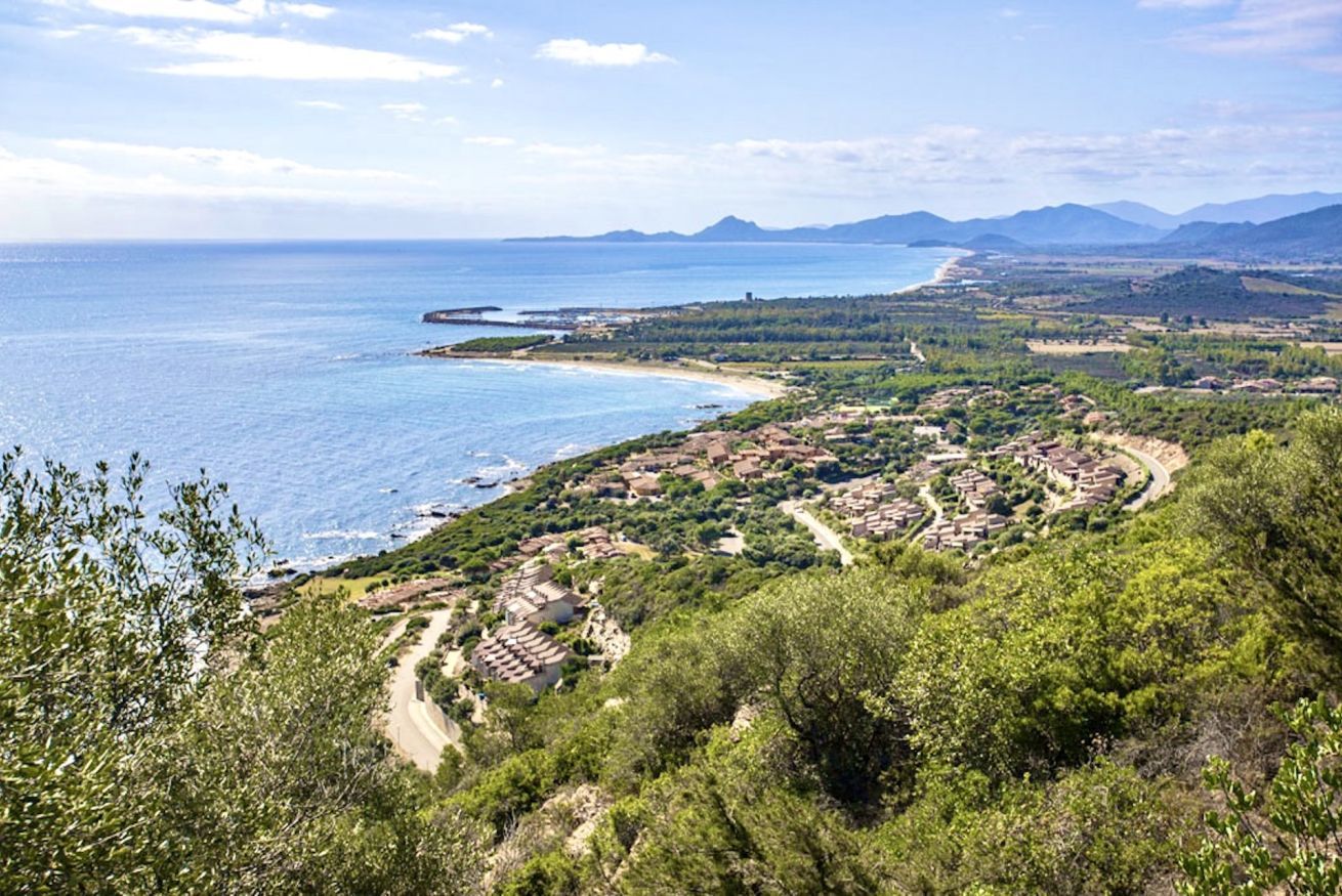 Un village côtier avec des maisons à étages, une plage et un paysage montagneux en arrière-plan.