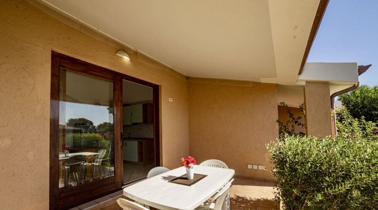 Un patio exterior con una mesa y sillas, una puerta corrediza de vidrio y una pequeña zona ajardinada.