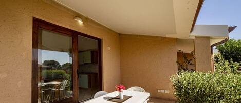 Un patio exterior con una mesa y sillas, una puerta corrediza de vidrio y una pequeña zona ajardinada.