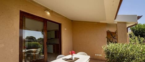 Un patio exterior con una mesa y sillas, un ventanal corredero y un pequeño jardín.
