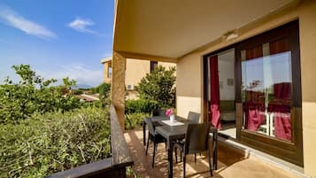 Un balcon avec une table et des chaises, une vue sur la verdure et un bâtiment en arrière-plan.