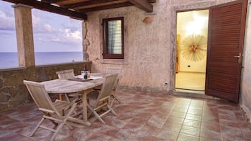 Une terrasse couverte avec une table et des chaises, une vue sur la mer et une porte donnant sur un espace intérieur.