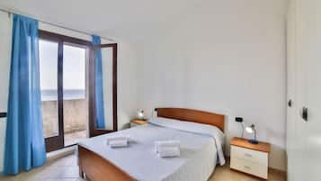 Une chambre à coucher avec un lit, une table de chevet, une lampe et une vue sur l’extérieur à travers une fenêtre avec des rideaux.
