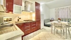 Eine kompakte Küche mit Gasherd, Spüle und moderner Küchenzeile. Es gibt eine Essecke mit Tisch und Stühlen, und im Hintergrund steht ein Sofa.