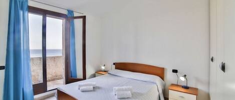 A bedroom with a bed, a nightstand, a lamp, and a view through a window with curtains.