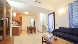 Ein modernes Wohnzimmer mit einer Couch, einem Esstisch mit Stühlen, einer Küchenzeile mit Schränken und einer Treppe, die zu einer oberen Etage führt.