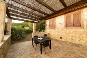An outdoor patio with a table and chairs, a pergola, and a stone wall.