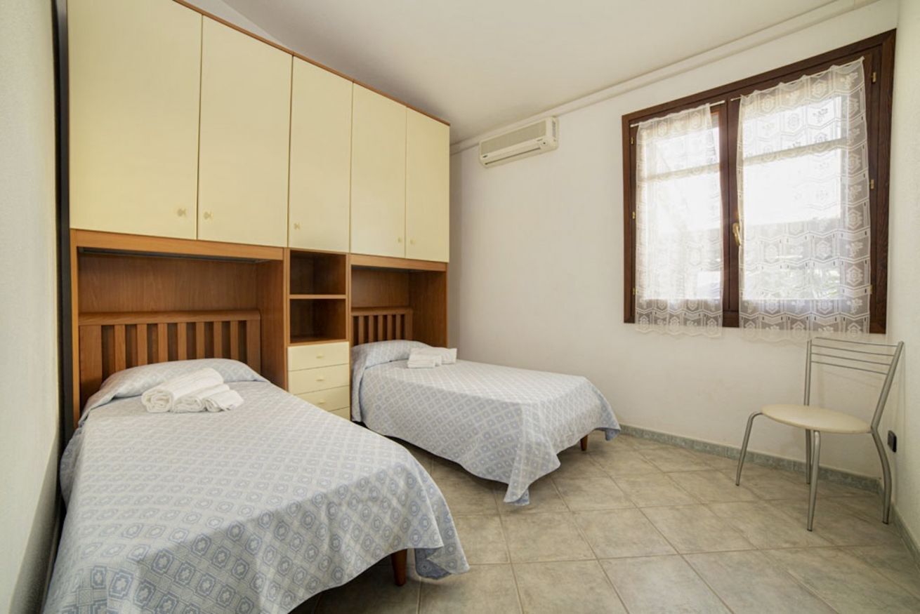 Un dormitorio con dos camas individuales, un armario, una silla y una ventana con cortinas estampadas.