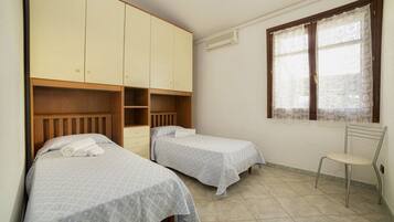 Un dormitorio con dos camas individuales, un armario, una silla y una ventana con cortinas estampadas.