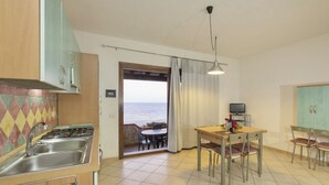A compact kitchen with a gas stove, sink, and a dining area with a table and chairs. A television is on a stand next to the table.