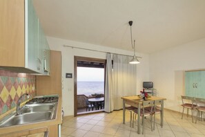 A compact kitchen with a gas stove, sink, and a dining area with a table and chairs. A television is on a stand next to the table.
