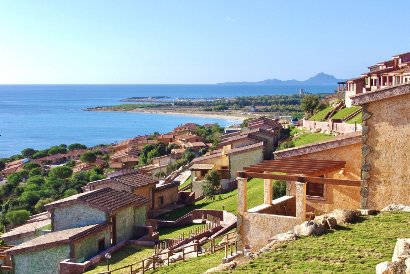 A coastal village with traditional stone buildings, a beach, and a mountainous backdrop.