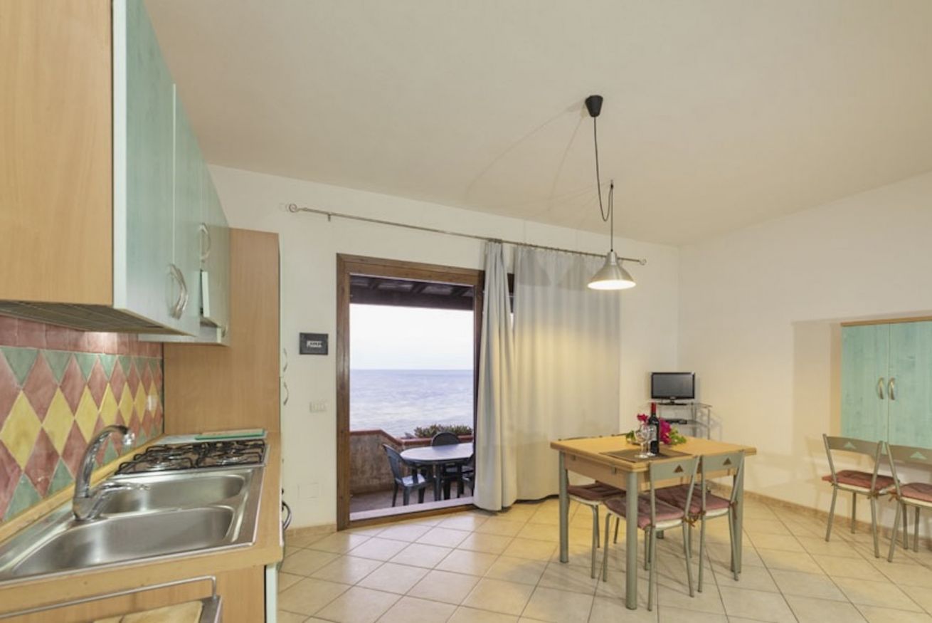 A compact kitchen with a gas stove, sink, and a dining area with a table and chairs. A television is on a stand next to the table.