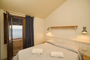 A bedroom with a bed, two bedside lamps, a nightstand, a window with curtains, and a view of the sea. - Porto Coral Villa, Sleeps 8 (Villaputzu)