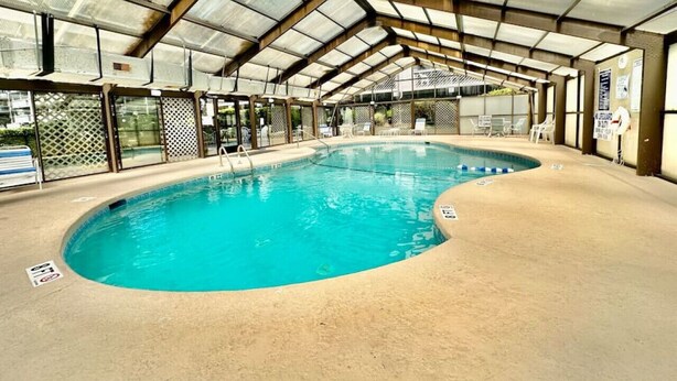 Una piscina interior de diseño curvo, rodeada de sillones de descanso y una estructura de techo cubierto.