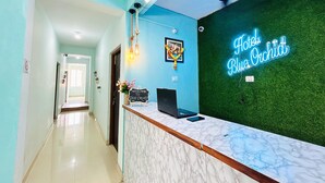 A hotel reception area with a marble counter, a neon sign reading "Hotel Blue Orchid," and a green wall with a welcome sign. - Blue Stay Inn Holiday Home - Near Baga Calangute Beach (Calangute)