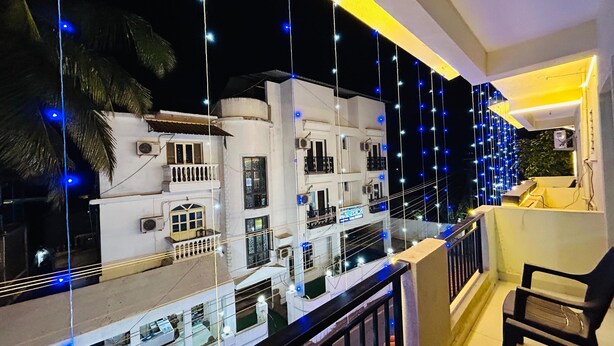 A balcony with a railing, a chair, and a view of a white building with multiple windows and balconies. - Blue Stay Inn Holiday Home - Near Baga Calangute Beach (Calangute)