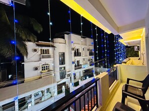 A balcony with a railing, a chair, and a view of a white building with multiple windows and balconies. - Blue Stay Inn Holiday Home - Near Baga Calangute Beach (Calangute)
